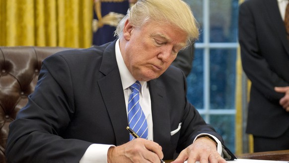 epa05744783 US President Donald J. Trump signs the last of three Executive Orders in the Oval Office of the White House in Washington, DC, USA, 23 January 2017. They concerned the withdrawal of the Un ...