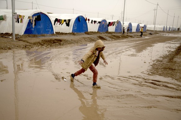 epa05656939 A displaced Iraqi child walks in the mud following heavy rain, at the Khazir camp, east of Mosul, northern Iraq, 02 December 2016. Iraqi forces started their military offensive to recaptur ...