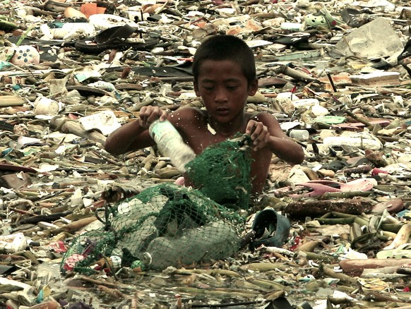 Ein Junge sammelt durchs Abfallwasser watend Plastikmüll ein, der vom Tropensturm Saola in die Buchten von Manila geweht wurde.