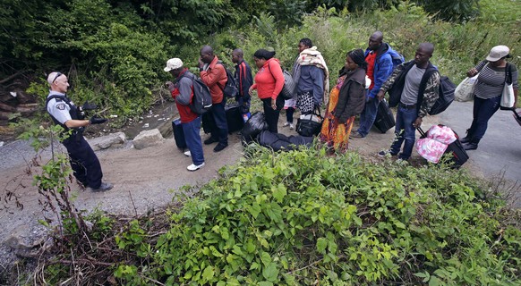 A Royal Canadian Mounted Police officer, left, standing in Saint-Bernard-de-Lacolle, Quebec, advises migrants that they are about to illegally cross from Champlain, N.Y., and will be arrested, Monday, ...