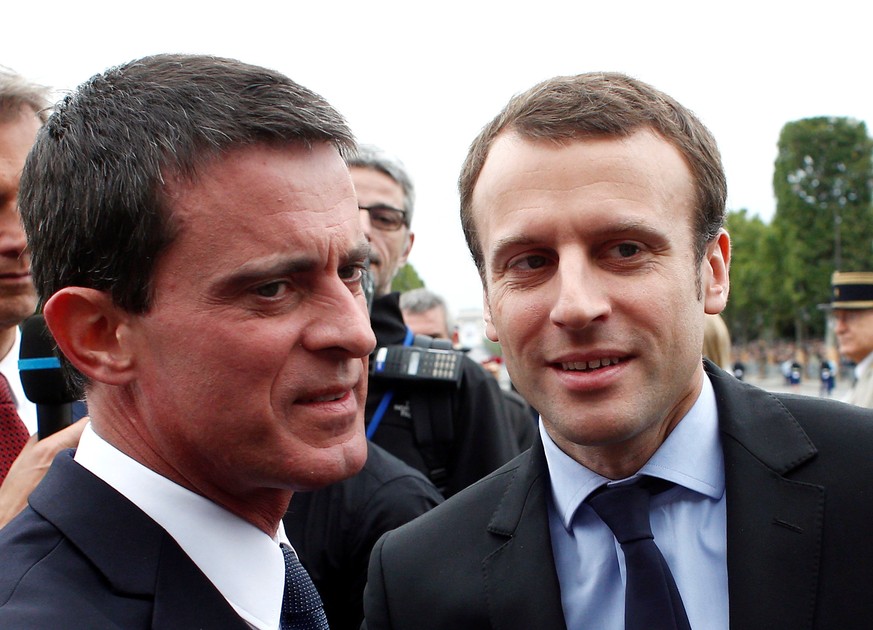 FILE PHOTO: French Prime Minister Manuel Valls (L) welcomes Economy Minister Emmanuel Macron on the Champs-Elysees Avenue before the Bastille Day military parade in Paris, France, July 14, 2016. REUTE ...