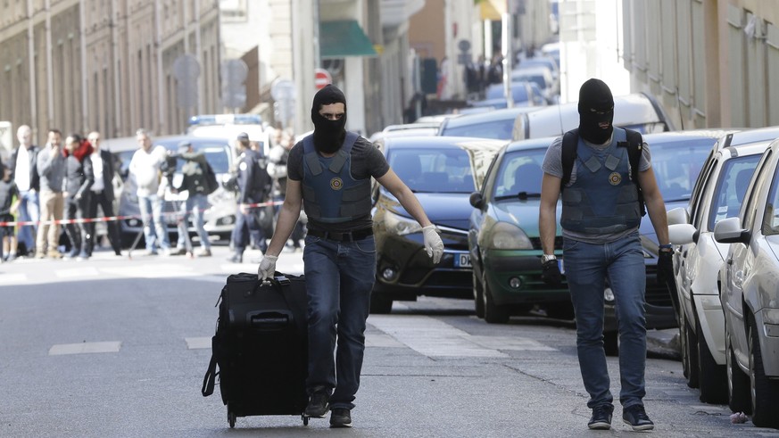 A hooded elite police officers pulls a suitcase after searches in Marseille, southern France, Tuesday, April 18, 2017. The French interior minister says police have arrested two suspected radicals who ...