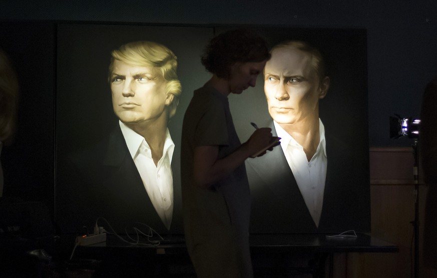 A journalist writes a material as she watches a live telecast of the U.S. presidential election standing at portraits of U.S. presidential candidate Donald Trump and Russian President Vladimir Putin i ...