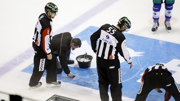 A technician tries to repair a hole into the ice past Head referee Stefan Eichmann, left, Linesmen Cedric Borga, and Head referee Micha Hebeisen, right, during the second period of the Swiss Ice Hocke ...