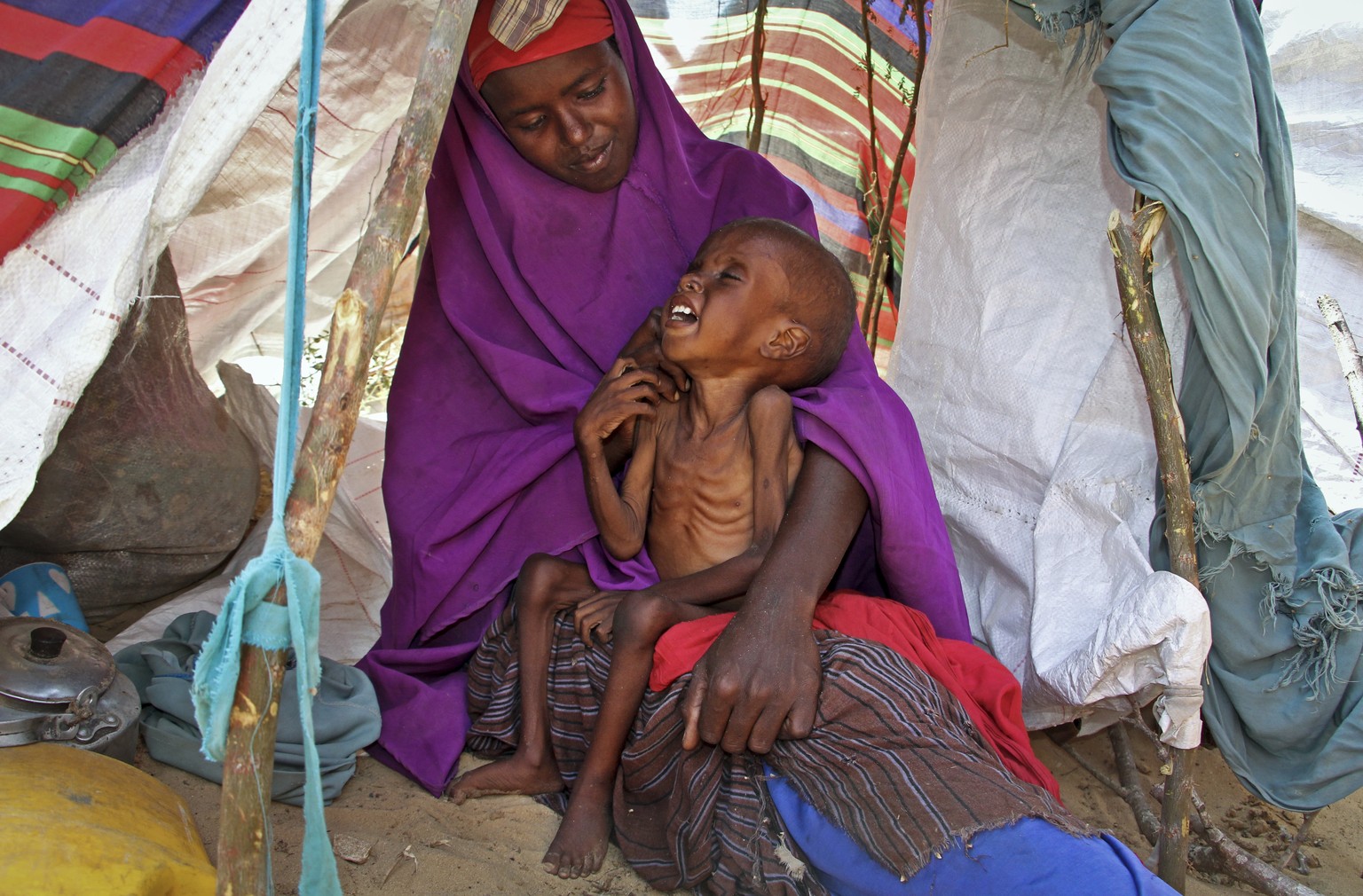 In this photo taken Tuesday, March 28, 2017, newly displaced Somali mother Sahra Muse, 32, comforts her malnourished child Ibrahim Ali, 7, in their makeshift shelter at a camp in the Garasbaley area o ...
