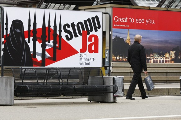 Ein Passant geht an einem Plakat vorbei, welches ein Minarettverbot in der Schweiz fordert, waehrend ein anderes, im Hintergrund, Touristen in der Schweiz willkommen heisst, am Montag, 26. Oktober 200 ...