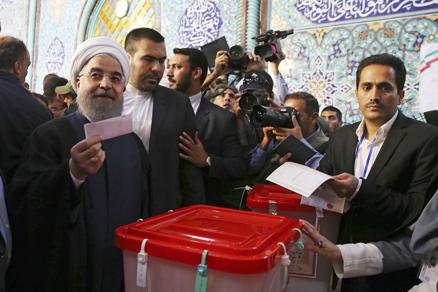 In this photo released by official website of the office of the Iranian Presidency, President Hassan Rouhani holds his ballot while voting for the presidential and municipal councils election at a pol ...