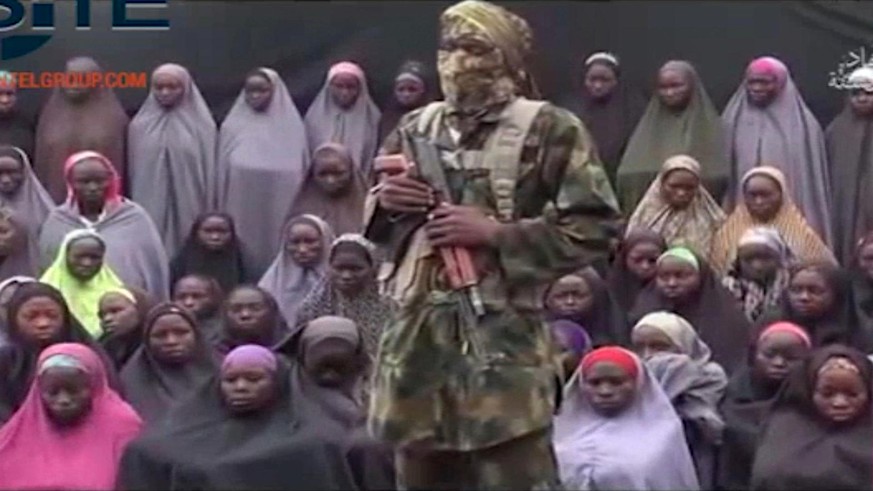 FILE- In this undated image taken from video distributed Sunday, Aug. 14, 2016, an alleged Boko Haram soldier standing in front of a group of girls alleged to be some of the 276 abducted Chibok school ...