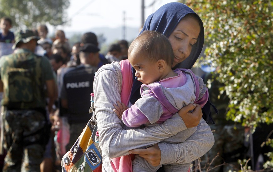 A woman migrant with a baby enters into Macedonia from Greece on the border line between the two countries, near southern Macedonia&#039;s town of Gevgelija, on Tuesday, Aug. 25, 2015. Thousands of mi ...