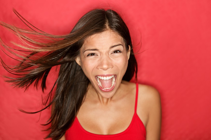 Scream. Woman screaming wild and crazy at full energy looking at camera on red background. Beautiful mixed race Asian Caucasian brunette female model with wind in the hair.
Horror, Angst, Schrei