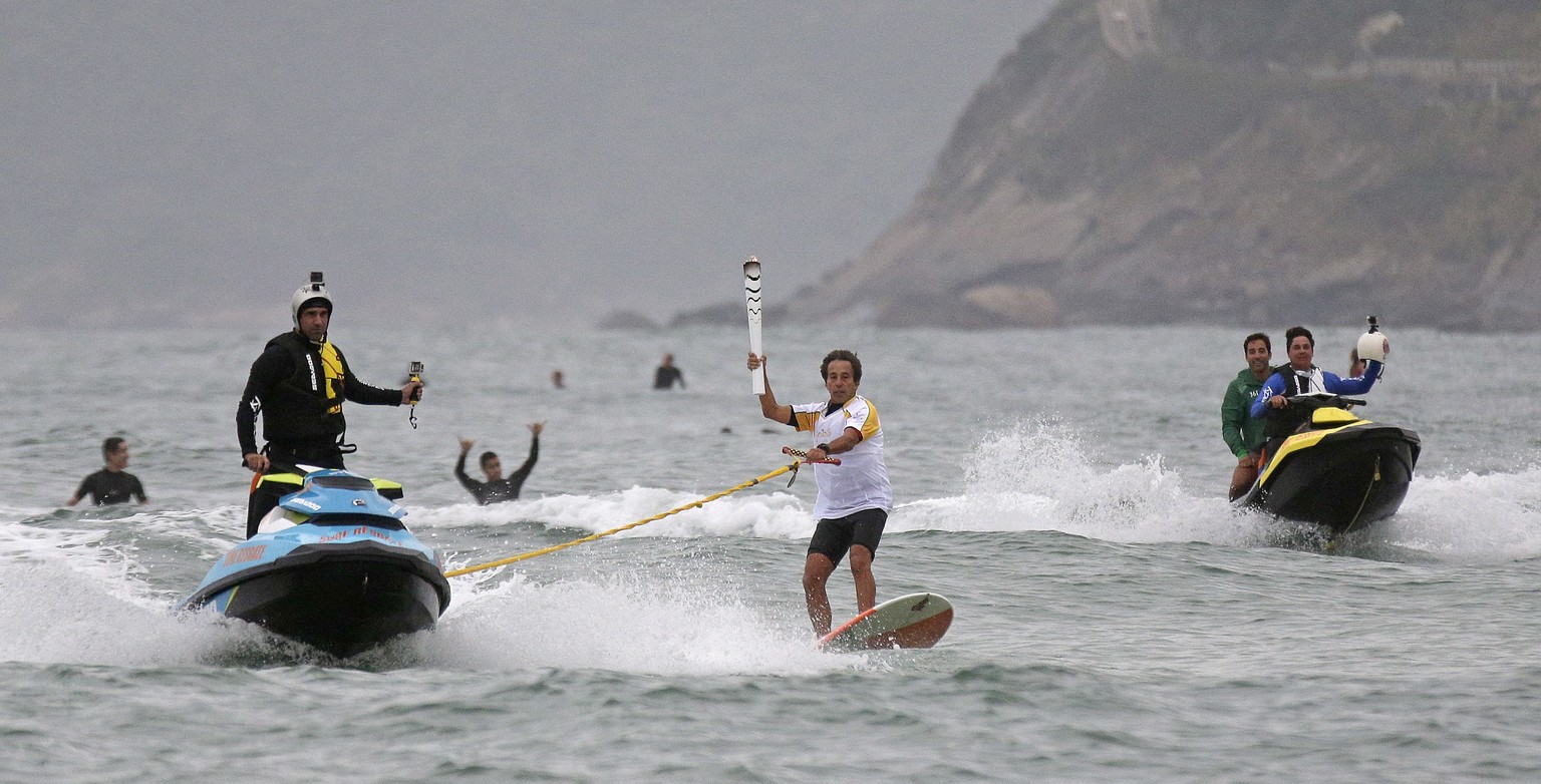 Brazilian Rico de Souza surfs with the Olympic torch at Macumba beach at Recreio dos Bandeirantes as torch relay continues on its journey to the opening ceremony of Rio&#039;s 2016 Summer Olympics, in ...