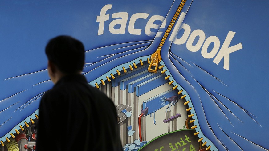 FILE - In this June 11, 2014, file photo, a man walks past a mural in an office on the Facebook campus in Menlo Park, Calif. Facebook is taking an aggressive new tack that blocks ad blockers on the de ...