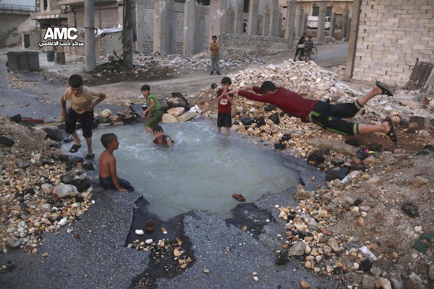FILE -- In this Aug. 31, 2016 file photo, provided by the Syrian anti-government activist group Aleppo Media Center (AMC), shows Syrian boys dive into a hole filled with water that was caused by a mis ...