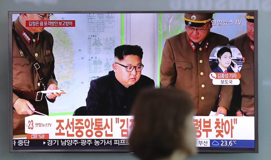 A woman walks by a TV screen showing a local news program reporting about North Korean military&#039;s plans to launch missiles into waters near Guam, with an image of North Korean leader Kim Jong Un, ...