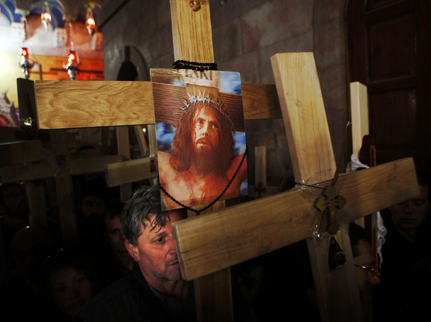 A Christian Orthodox pilgrim holds a cross with a hologram of Jesus Christ as he waits to enter Calvary during Good Friday processions in the Church of the Holy Sepulcher, traditionally believed to be ...