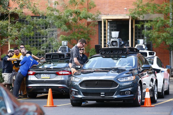 Uber employees stand by self-driving Ford Fusion hybrid cars during testing of the vehicles, Thursday, Aug. 18, 2016, in Pittsburgh. Uber said that passengers in Pittsburgh will be able to summon ride ...
