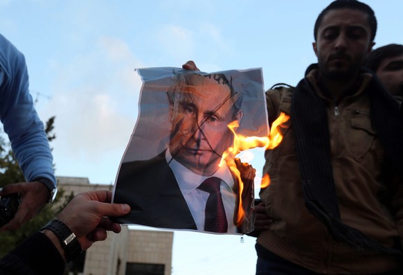 epa05674157 Protesters burn a photo of Russian President Vladimir Putin during a protest in front of Russian embassy in Amman, Jordan, 13 December 2016. Protesters gathered to urge the international c ...