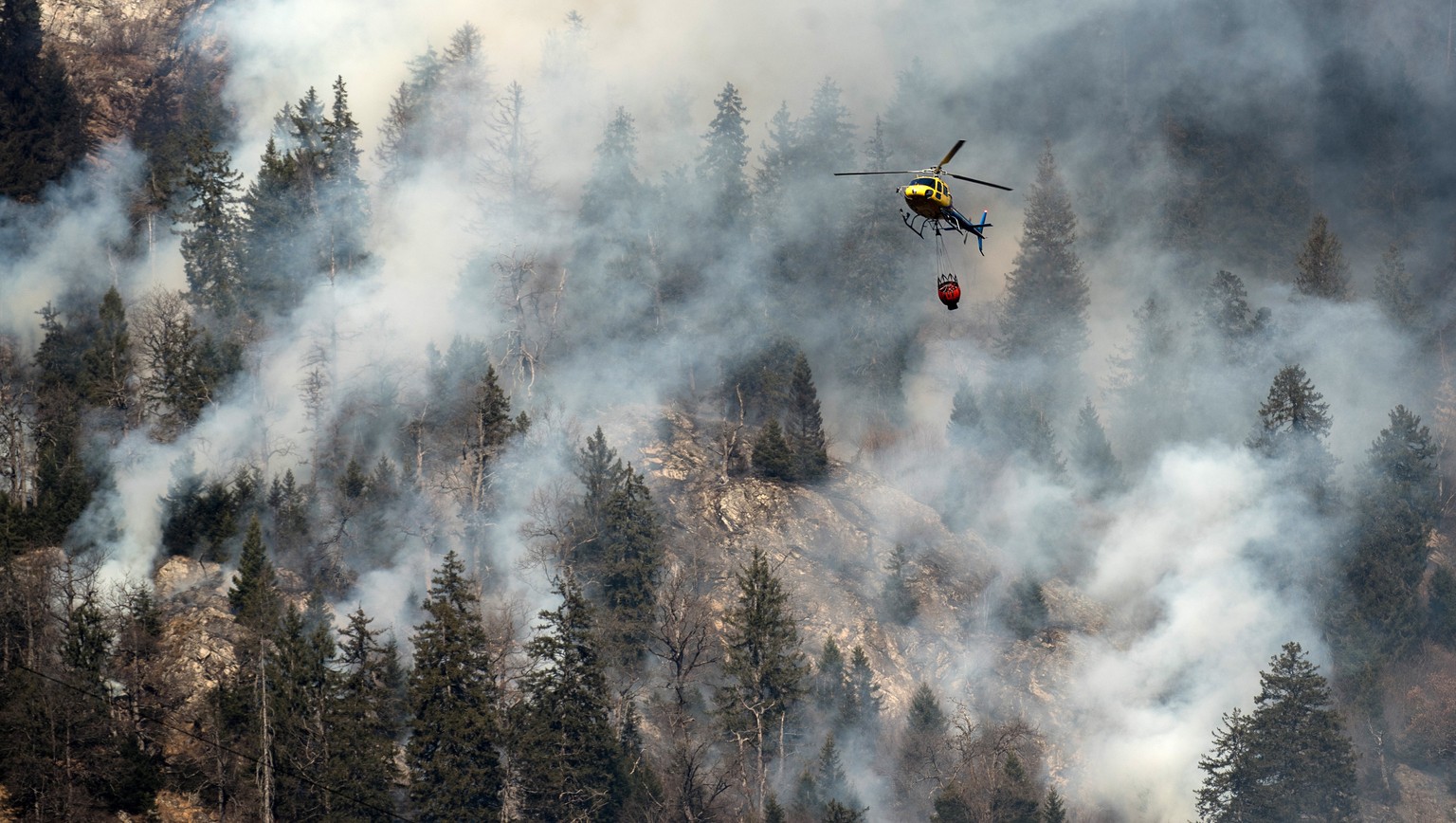 A fire fighting helicopter discharges water over the forest fires near Mesocco in Southern Switzerland, Wednesday, December 28, 2016. (KEYSTONE/Ti-Press/Gabriele Putzu)