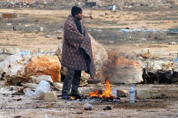 This image released on Friday, Dec. 16, 2016 by Aleppo 24, shows a man of eastern Aleppo standing next to a fire in western rural Aleppo, Syria. As the last holdouts leave the rebel-held enclave in Al ...