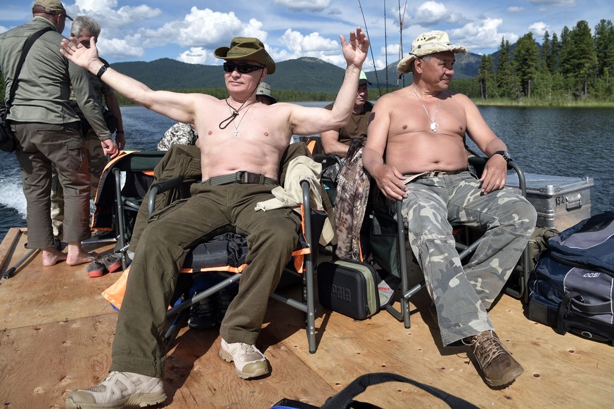 In this photo released by Kremlin press service on Saturday, Aug. 5, 2017, Russian President Vladimir Putin, left, and Defense Minister Sergei Shoigu rest after fishing during a mini-break in the Sibe ...