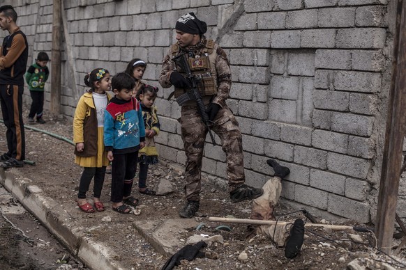 In this Sunday, Dec. 18, 2016 photo, Iraqi children look at the body of a half-buried Islamic State militant while talking to an Iraqi soldier in the al-Barid district in Mosul, Iraq. In a part of Mos ...