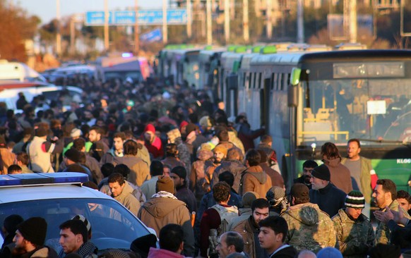 This image released on Thursday, Dec. 15, 2016 by Aleppo 24, shows residents gathered near green government buses as they hold their belongings for evacuation from eastern Aleppo, Syria. As the last h ...