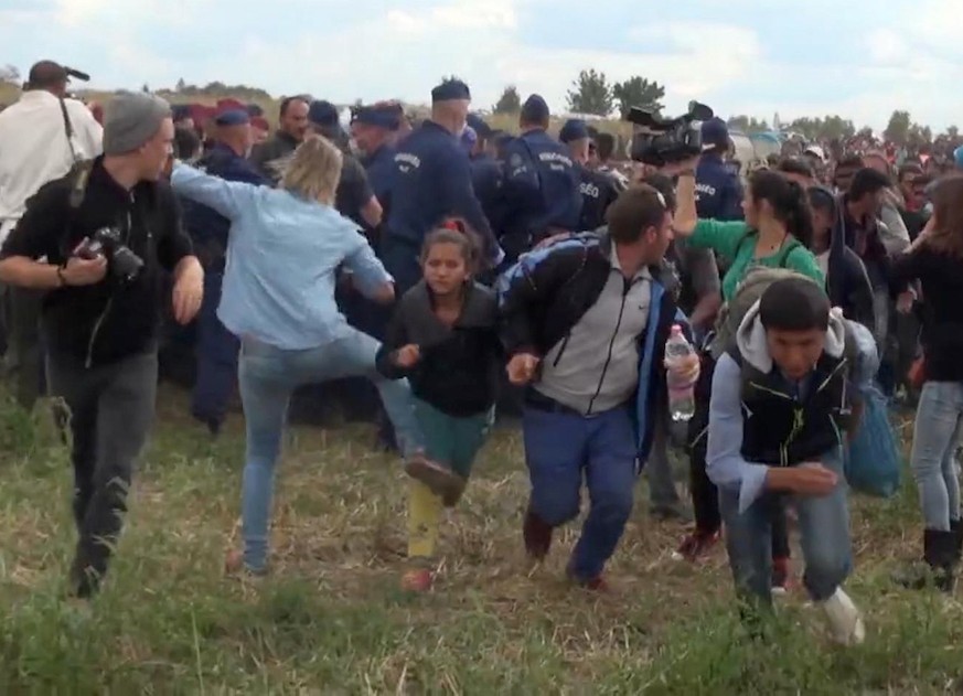 In this image taken from TV a Hungarian camerawoman, center left in blue, kicks out at a young migrant who had just crossed the border from Serbia near Roszke Hungary Tuesday Sept. 8, 2015. The camera ...