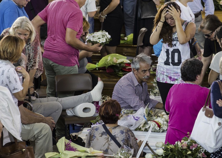 A woman holds her head as she looks at a coffin laid out in state, Saturday, Aug. 27, 2016, before the start of the mass funerals in Ascoli Piceno, central Italy, for some of the victims of a major ea ...