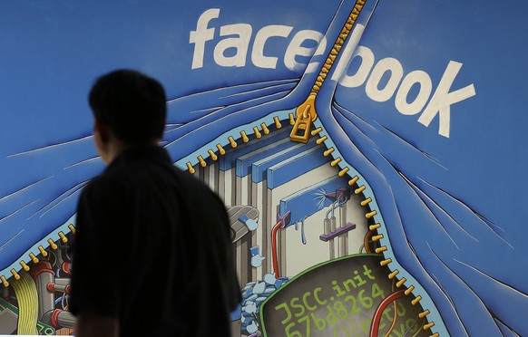 FILE - In this June 11, 2014, file photo, a man walks past a mural in an office on the Facebook campus in Menlo Park, Calif. Facebook is taking an aggressive new tack that blocks ad blockers on the de ...
