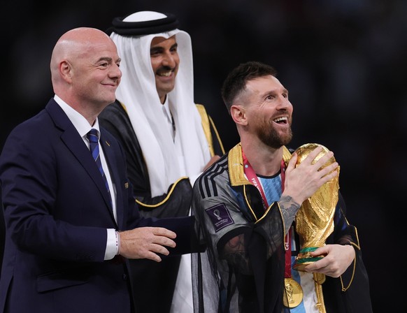 epa10373010 Lionel Messi (R) of Argentina celebrates with the World Cup trophy next to Tamim bin Hamad Al Thani (C), the Emir of Qatar, and FIFA President Gianni Infantino (L) during the trophy ceremo ...