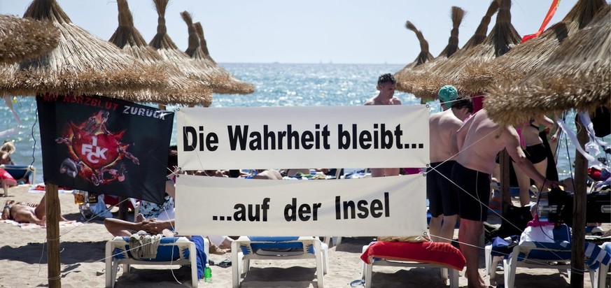 German tourists stand next to a poster saying &quot;The truth stays on the island&quot; at the beach in Platja de Palma on the Spanish island Mallorca, pictured on June 4, 2010. (KEYSTONE/Ennio Leanza ...