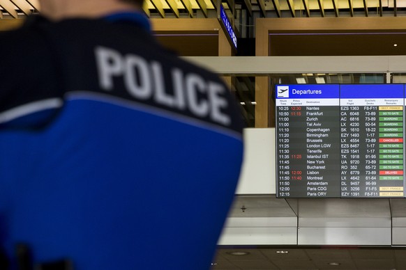 A police man stands in front of the panel with announcing cancelled flights to brussels at the Airport of Geneva, Switzerland, Tuesday, 22 March 2016. All flights to brussels are canceled following te ...