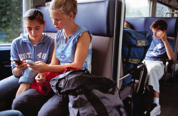 Zwei Maedchen beschaeftigen sich im Zug mit ihren Mobiltelefonen, aufgenommen am 29. August 2003 auf der Strecke Entlebuch-Schuepfheim. (KEYSTONE/Martin Ruetschi) === , === : DIA]