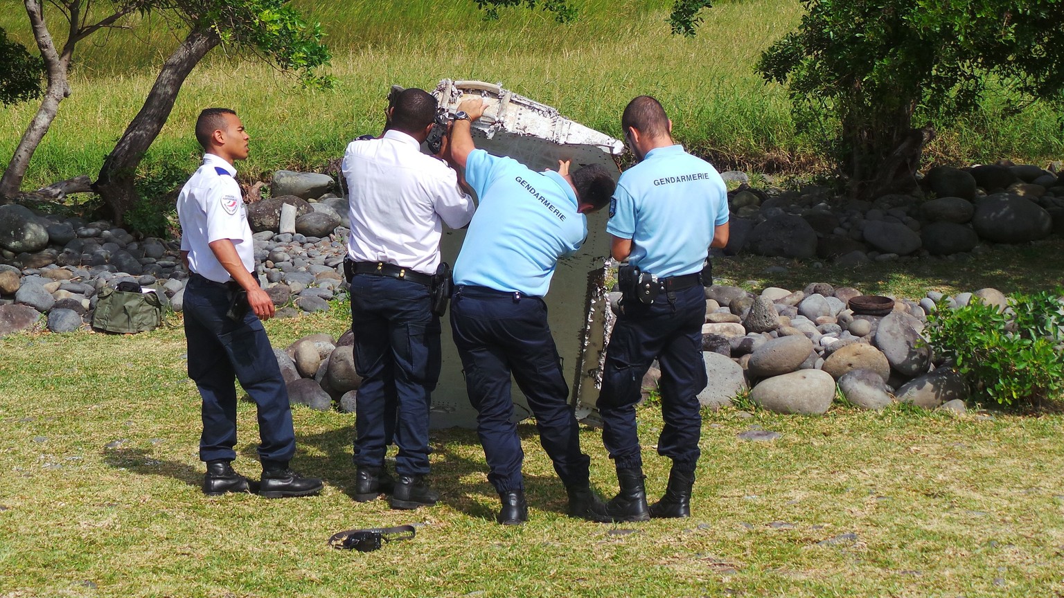 epa04866272 A picture made available 30 July 2015 shows members of French Gendarmerie and local authorities checking a piece of debris from an unidentified aircraft apparently washed ashore in Saint-A ...