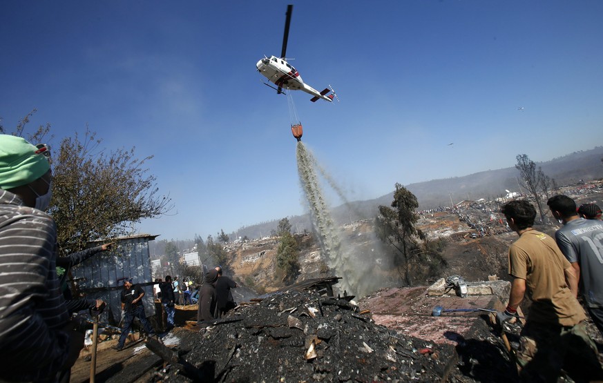 epa04167629 A helicopter releases water over a zone at Ramaditas hill in Valparaiso, Chile, on 14 April 2014. The fire, which has so far killed 12 people and destroyed more than 2,000 homes, began on  ...