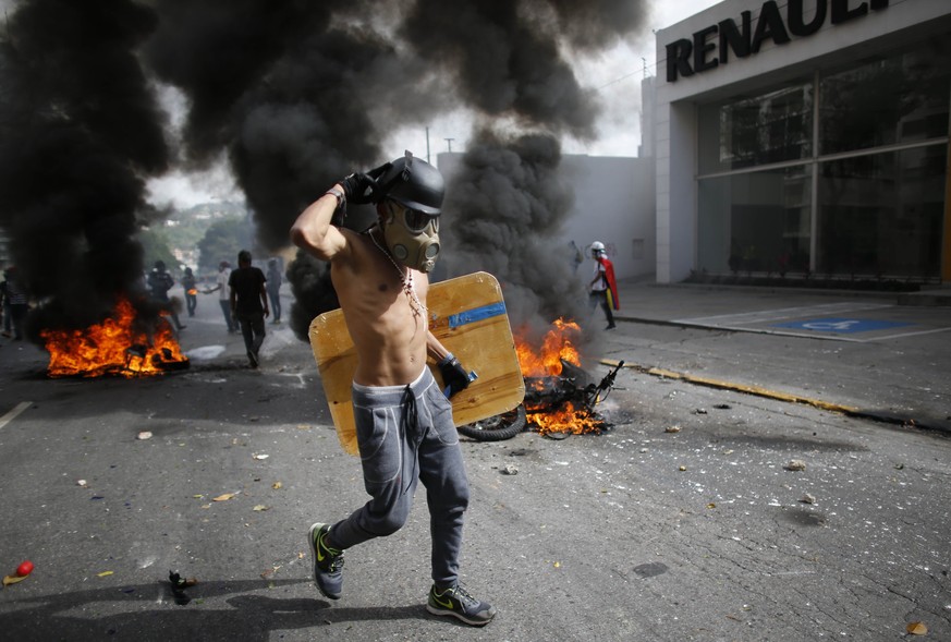 An anti-government demonstrator walks past two National Guard soldiers&#039; motorcycles that were set on fire by protesters when the soldiers ran from their bikes after falling during clashes with pr ...