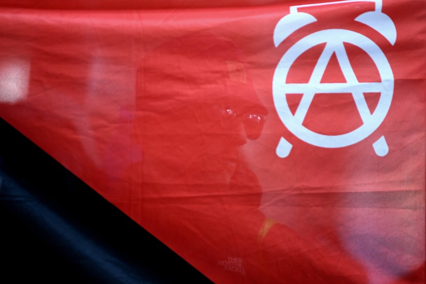 epa06069142 A protester is seen behind a banner showing an anarchist symbol as he arrives at Hamburg Hauptbahnhof central railway station ahead of the G20 Summit in Hamburg, Germany, 06 July 2017. The ...