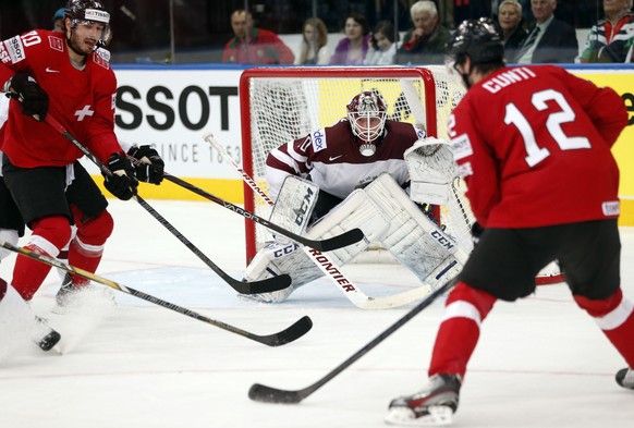 Switzerland forward Denis Hollenstein, left, and forward Luca Cunti, right, attempts to score past Latvia goaltender Kristers Gudlevskis during the Group B preliminary round match between Switzerland  ...