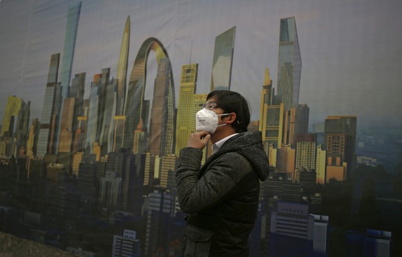 epa04495198 A man adjusts his mask to protect against smog beside a billboard featuring an artist impression of clear weather over Beijing, China, 19 November 2014. Smog has once again engulfed Beijin ...