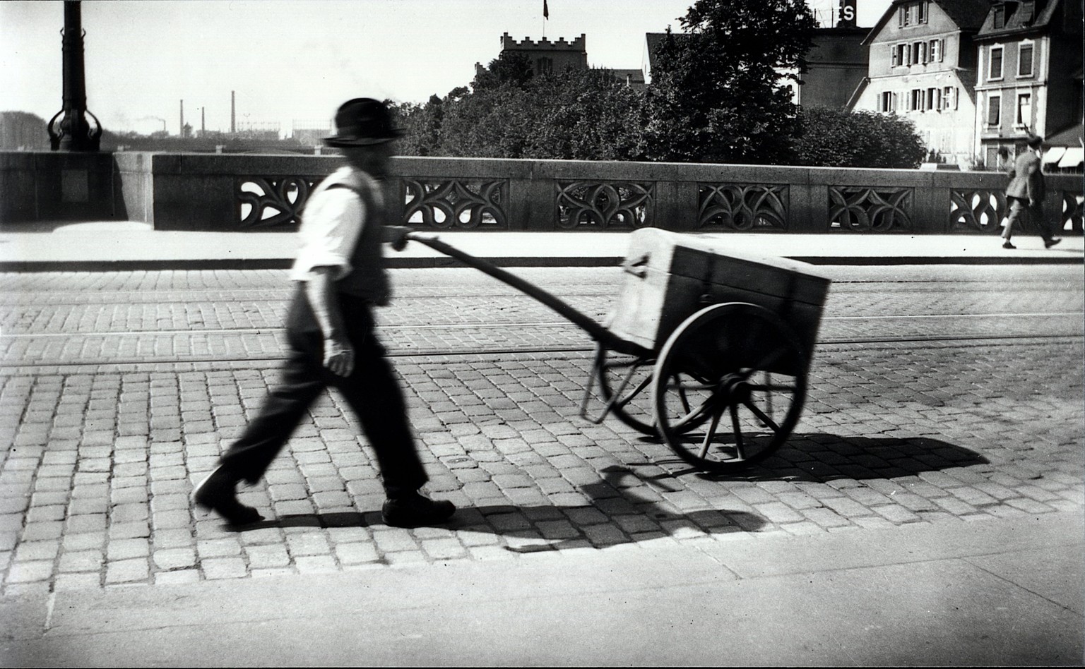 Ein Arbeiter stösst einen Karren mit Abfall, das aus Abwasserschächten stammt, über die mittlere Rheinbrücke von Gross- nach Kleinbasel im Jahre 1899.