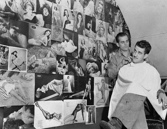 18 May 1944 --- A variation of the old Police Gazette, that used to keep customers happy in grandfather&#039;s day, is this collection of pinup cuties adorning the wall of this barber shop at a U.S. M ...