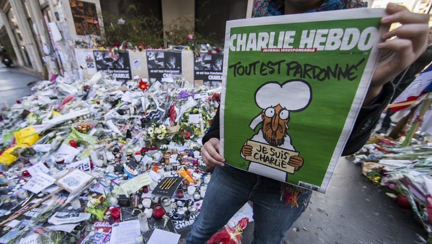 epa04559471 A woman holds the new edition of the French satirical magazine Charlie Hebdo in front of the improvised memorial on Rue Nicolas Appert, near the Charlie Hebdo headquarters, site of the 07  ...