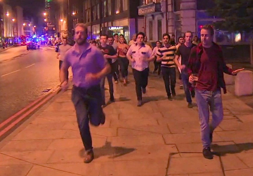 In this image taken from video footage, people run from the scene of attack, alongside a man strolling holding a pint of beer, right, in London, late Saturday, June 3, 2017. People in the U.K. have re ...