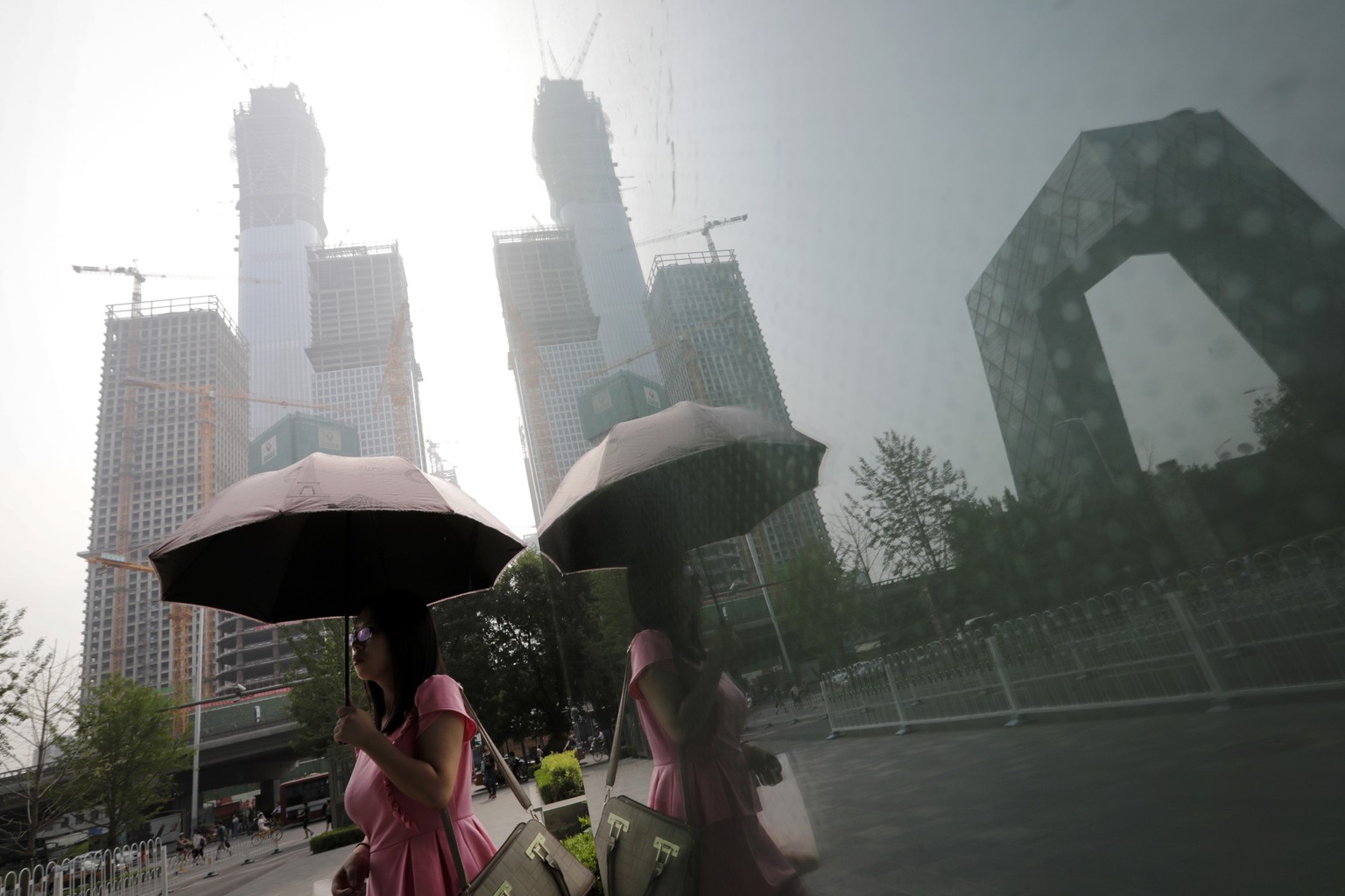 A woman carries an umbrella past a shopping mall&#039;s window with reflection of construction buildings at the Central Business District in Beijing, Monday, July 17, 2017. China&#039;s economic growt ...