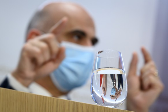 Bundesrat Alain Berset spiegelt sich in einem Glas Wasser an einer Medienkonferenz des Bundesrates zur aktuellen Lage im Zusammenhang mit dem Coronavirus, am Freitag, 5. Maerz 2021. (KEYSTONE/Anthony  ...