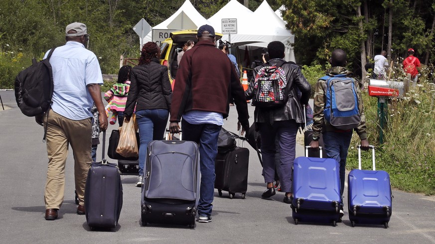 A family from Haiti approach a tent in Saint-Bernard-de-Lacolle, Quebec, stationed by Royal Canadian Mounted Police, as they haul their luggage down Roxham Road in Champlain, N.Y., Monday, Aug. 7, 201 ...