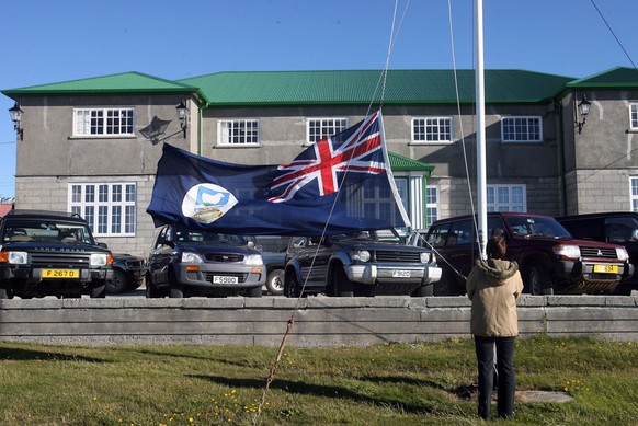 Ein Mann hisst vor einem Regierungsgebäude auf&nbsp;Port Stanley die Flagge der Falklandinseln.