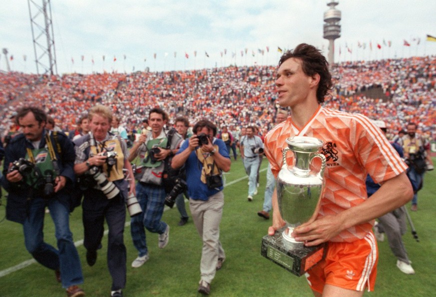 Der niederlaendische Stuermer Marco van Basten (r) traegt gluecklich den eroberten EM-Pokal auf einer Ehrenrunde ueber das Feld, und eine Gruppe von Fotografen hetzt hinterher. Die Fussballnationalman ...