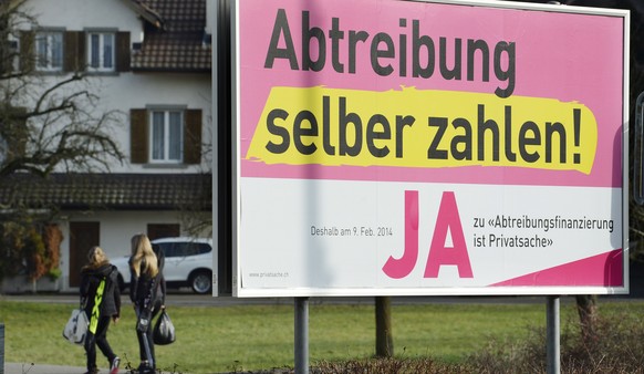 Passantinnen gehen an einem Plakat mit der Aufschrift &quot;Abtreibung selber zahlen-JA&quot; der Befuerworter der Abtreibungsfinanzierungsinitiative vorbei, aufgenommen am Sonntag, 12.Januar 2014, in ...