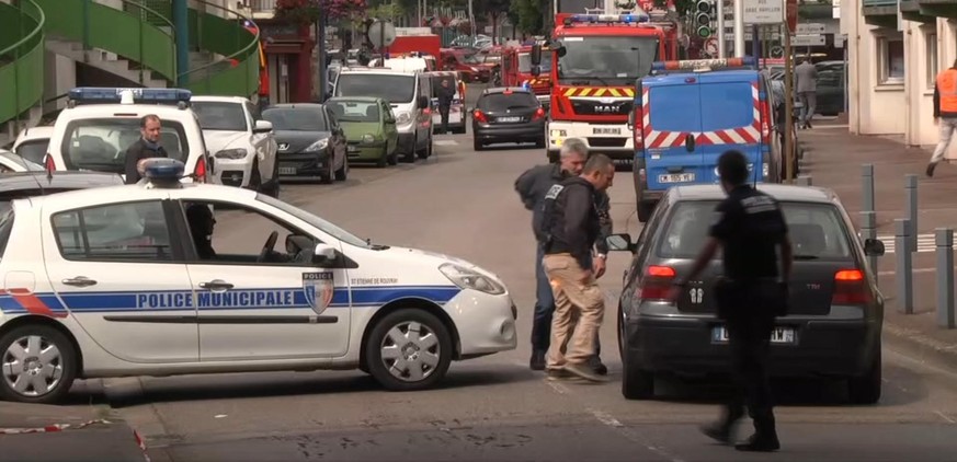 In this grab made from video, police officers speak to a driver as they close off a road during a hostage situation in Normandy, France, Tuesday, July 26, 2016. Two attackers seized hostages in a chur ...